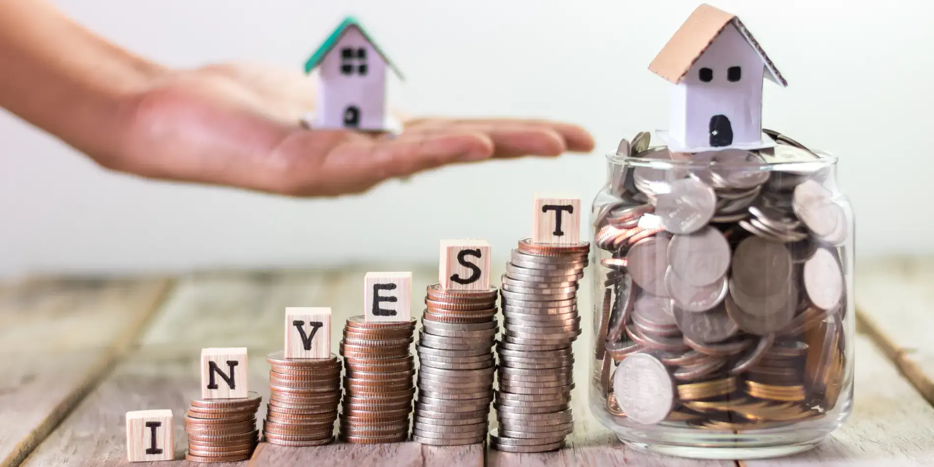 stack of coins with hand holding model house in background