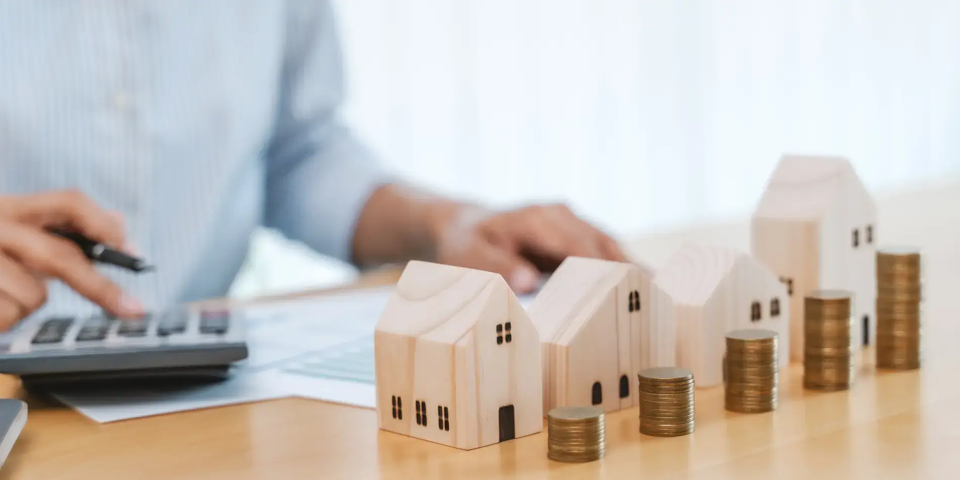 man in business shirt with models wooden houses and stacks of gold coins